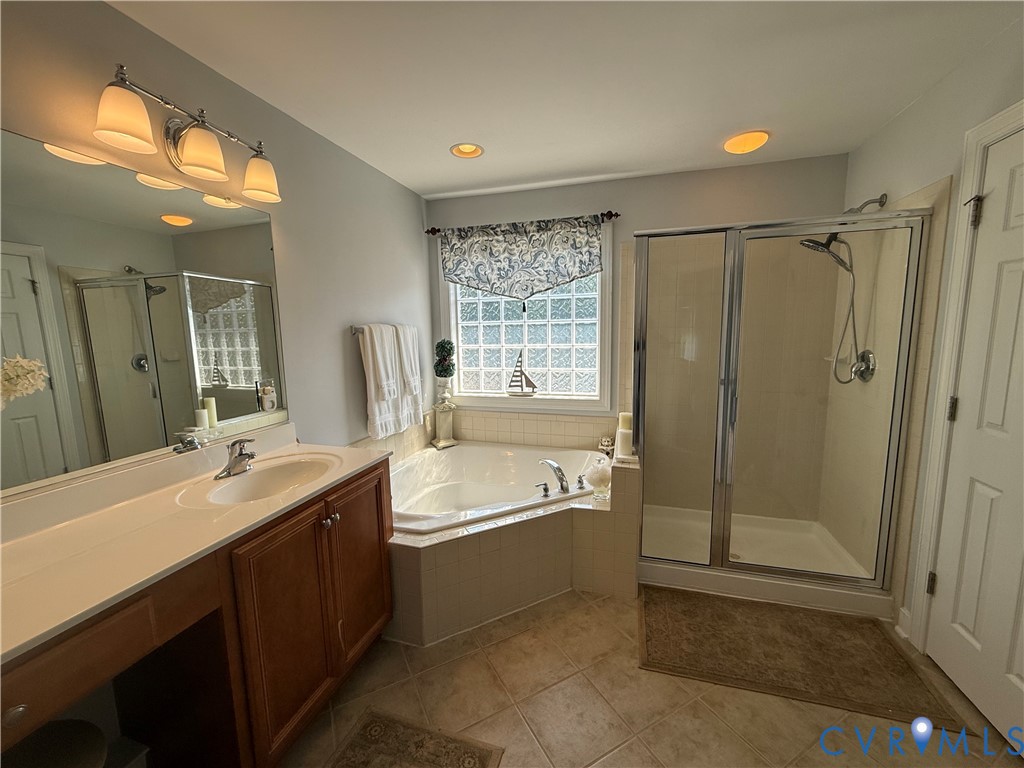 Bathroom featuring a double vanity with light wood cabinetry, an integrated soaking tub, a glass-enclosed shower, and a privacy glass block window
