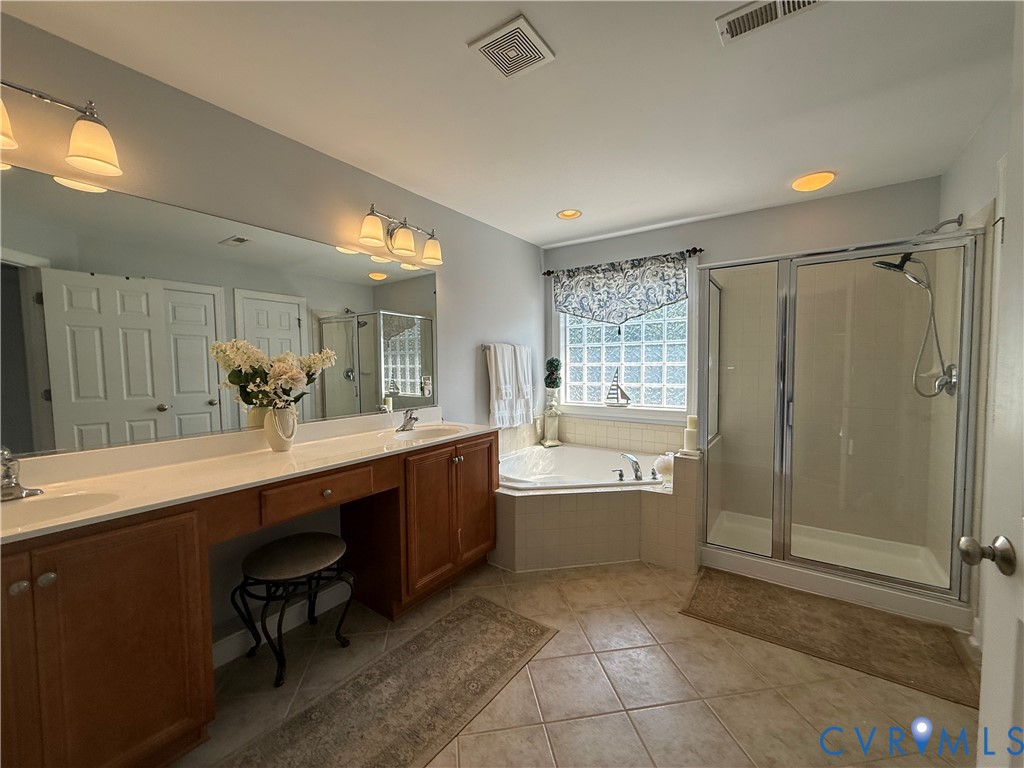 Spacious bathroom featuring an expansive double vanity with integrated sinks, a built-in vanity desk, a corner soaking tub, and a glass-enclosed shower