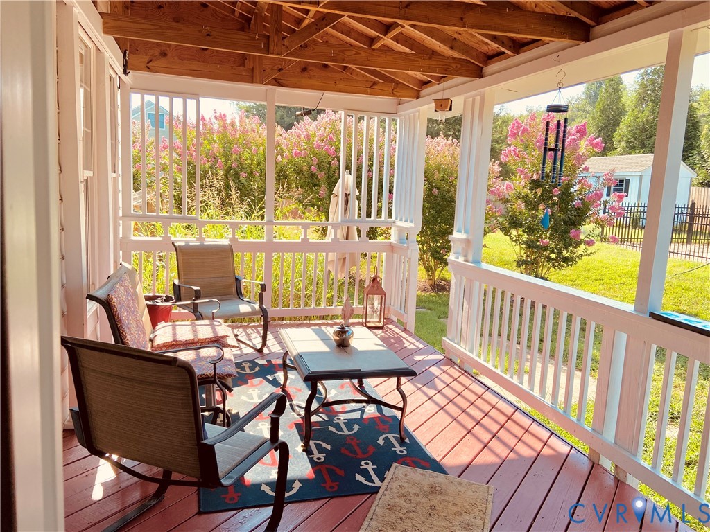 Covered porch featuring a red-stained wood-finish floor, white painted railings, exposed wood ceiling beams, and a lush green lawn beyond