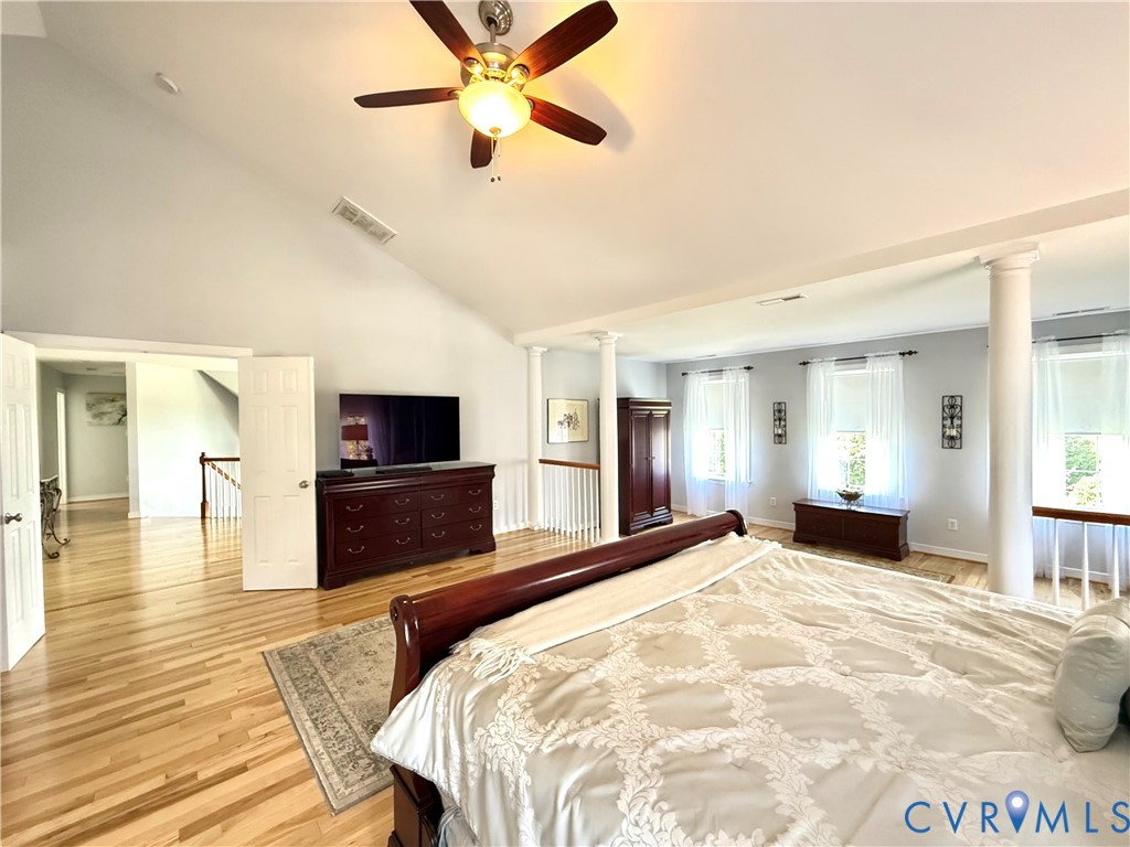 Vaulted ceiling with a ceiling fan, hardwood flooring, multiple windows, and decorative columns