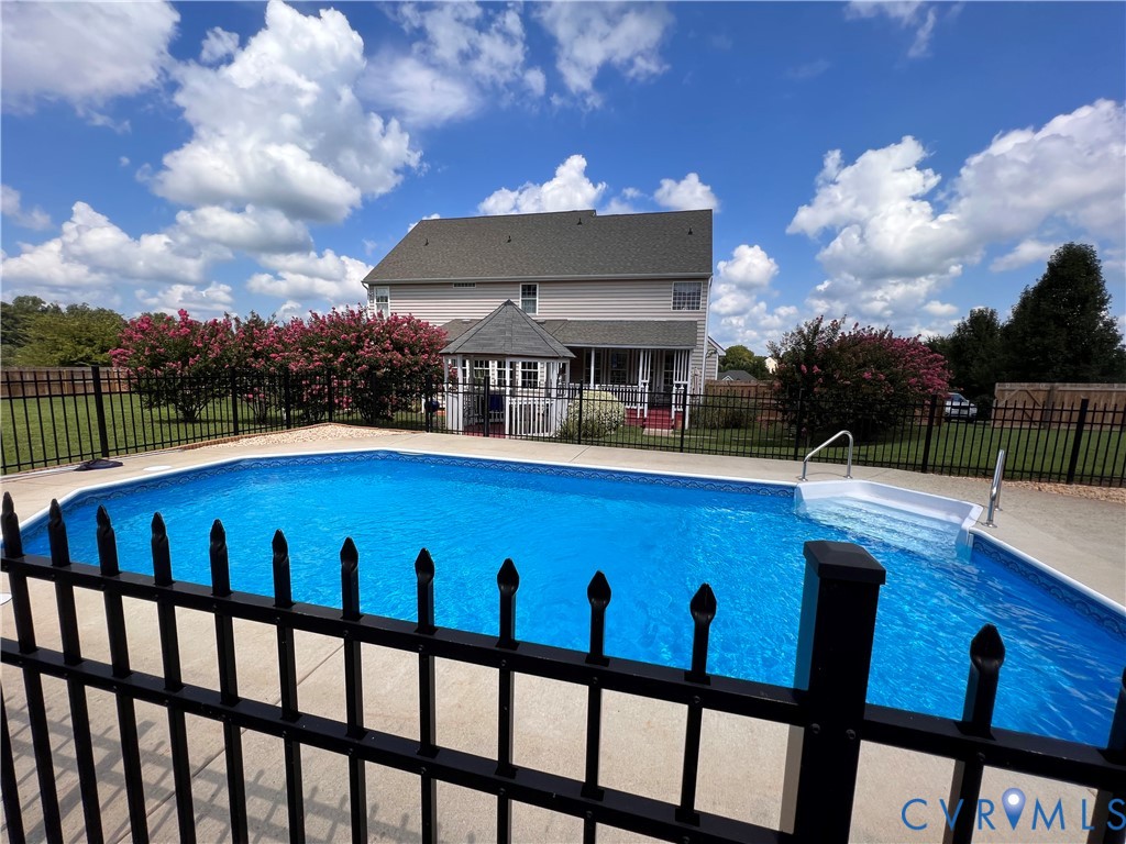In-ground swimming pool featuring broad steps, a surrounding concrete deck, and black wrought iron fencing