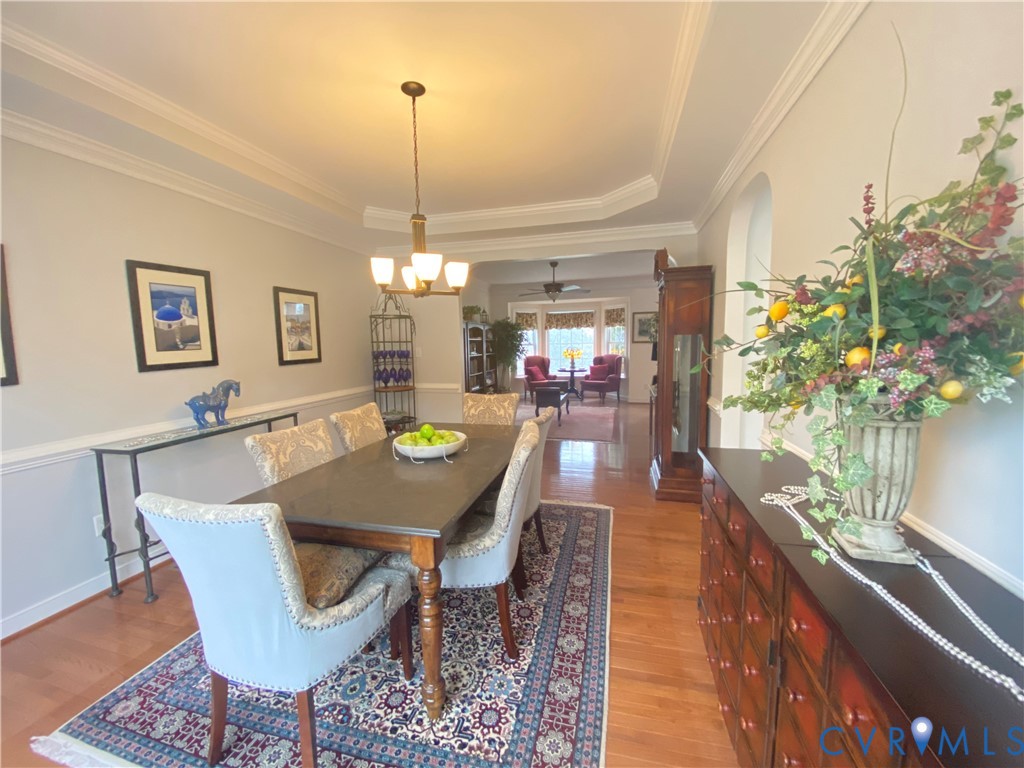 Formal dining area featuring hardwood flooring, a tray ceiling, crown molding, chair rail, and an archway leading to an additional living space