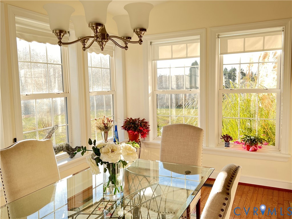 Dining area featuring a five-light chandelier, multiple double-hung windows, light-colored walls, and wood-finish flooring