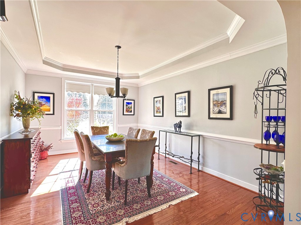Formal dining space featuring wood-finish flooring, tray ceiling with crown molding, and wainscoting