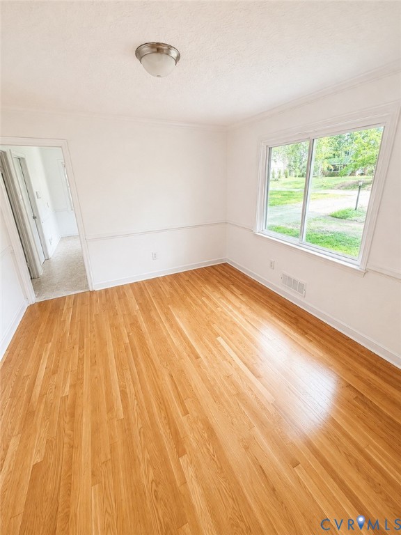 Hardwood flooring throughout, featuring a large window, a two-tone wall treatment, crown molding, and a flush mount ceiling light