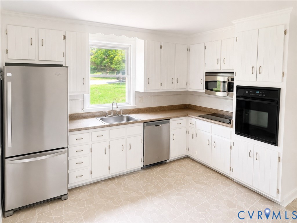Kitchen featuring white cabinetry, light-toned countertops, a stainless steel refrigerator, and a built-in oven with a microwave