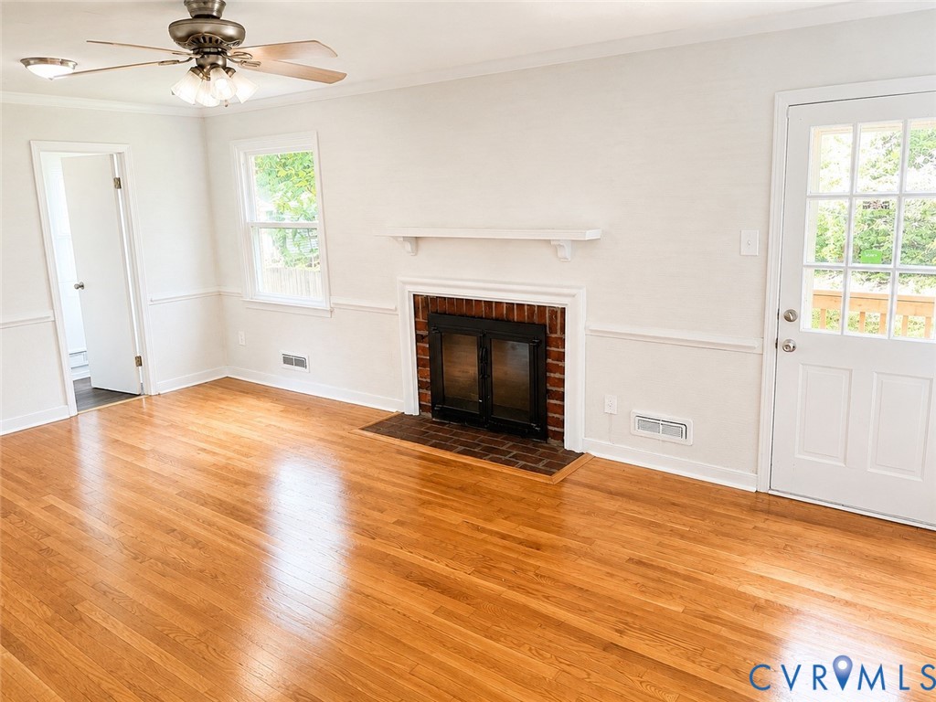 Bright interior featuring polished wood flooring, a brick fireplace with a white mantel, and a multi-pane glass-insert door