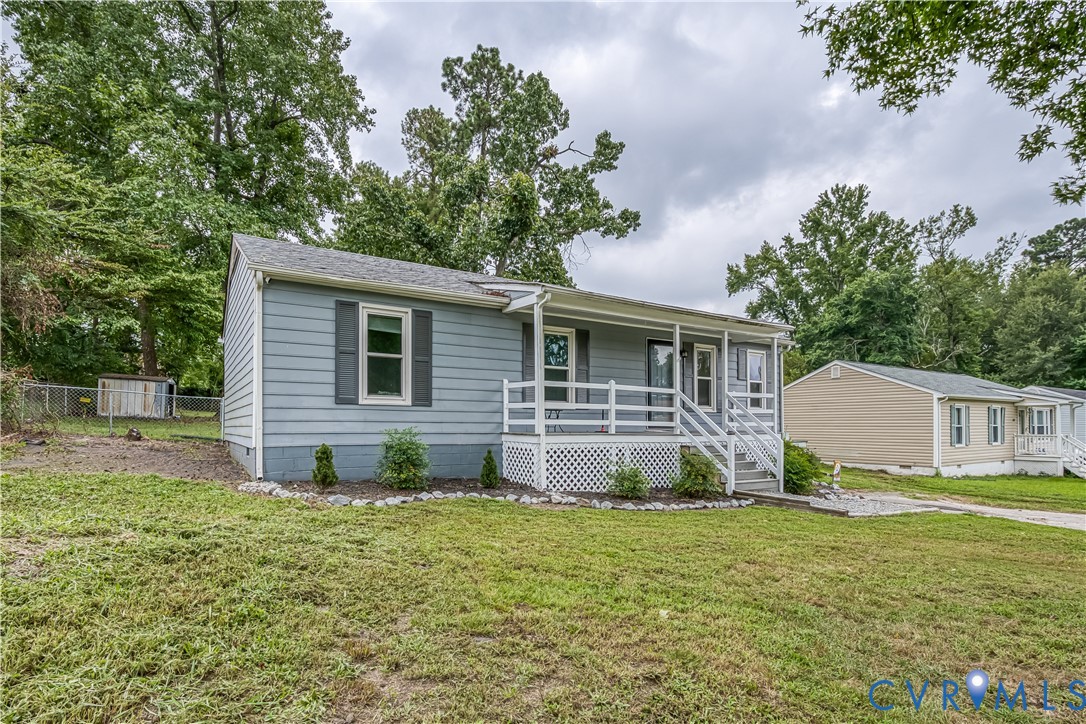Light blue siding exterior with dark gray shutters, a white railing porch, a gravel pathway, and a grassy front yard