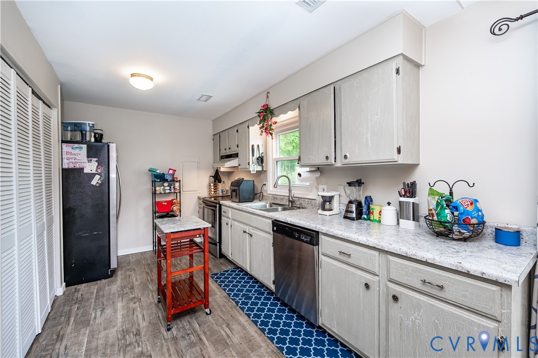 Kitchen featuring light gray cabinetry, speckled countertops, stainless steel dishwasher, and wood-finish flooring