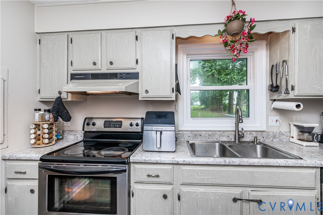 Kitchen featuring light-toned cabinetry, stainless steel oven with cooktop, stainless steel double basin sink with high-arc faucet, speckled countertops, and a window