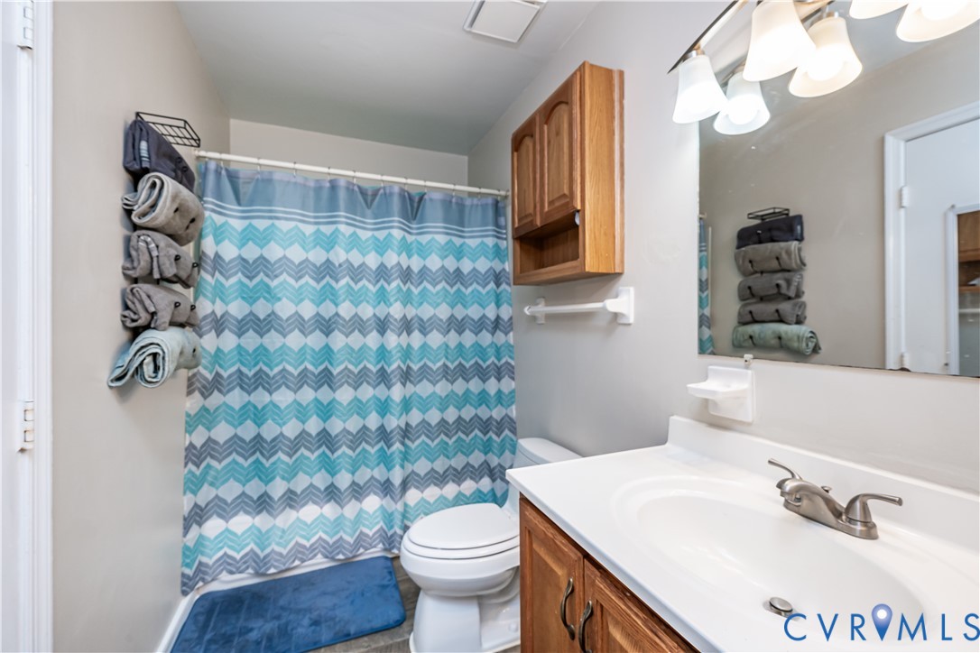 Full bathroom featuring a white vanity with integrated sink, wood-finish cabinetry, brushed nickel faucet, and an overhead mirror with vanity lighting