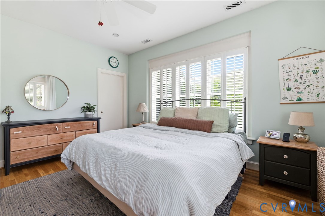 Spacious room featuring wood-finish flooring, white plantation shutters, and a ceiling fan