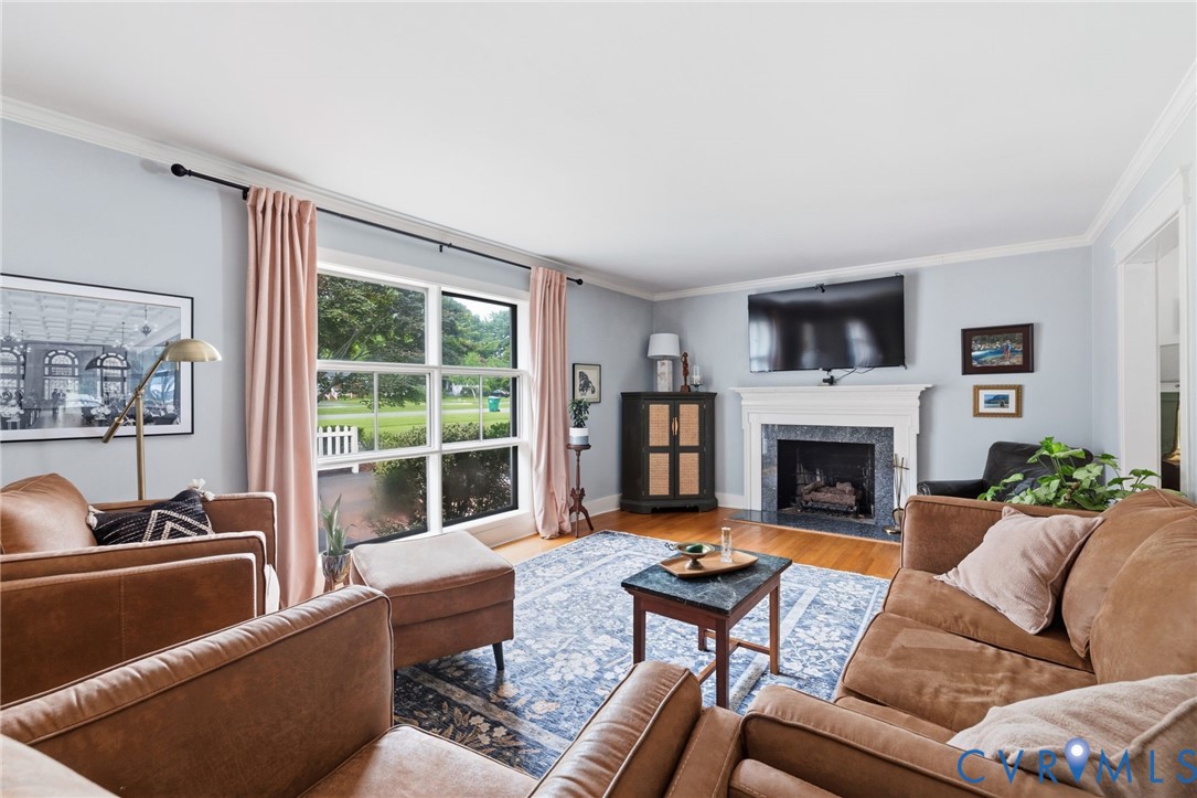 Spacious living area featuring polished wood flooring, a fireplace with a stone surround and a white mantel, and crown molding