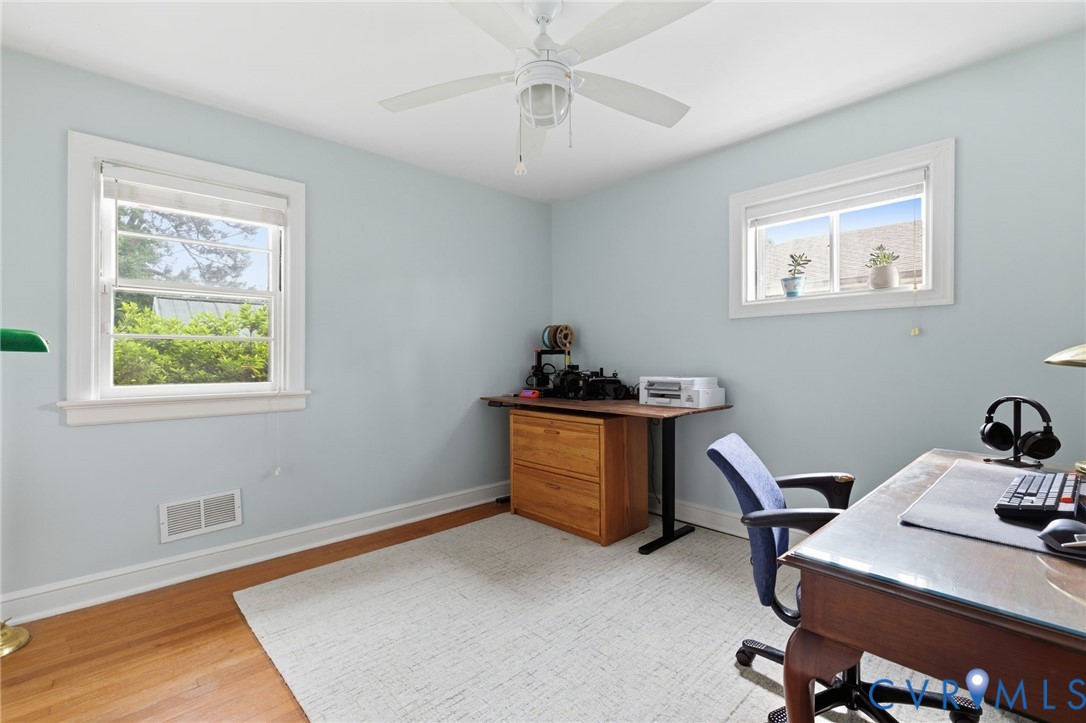 Light blue painted room featuring two windows, a white ceiling fan with integrated lighting, wood-finish flooring, and white baseboards