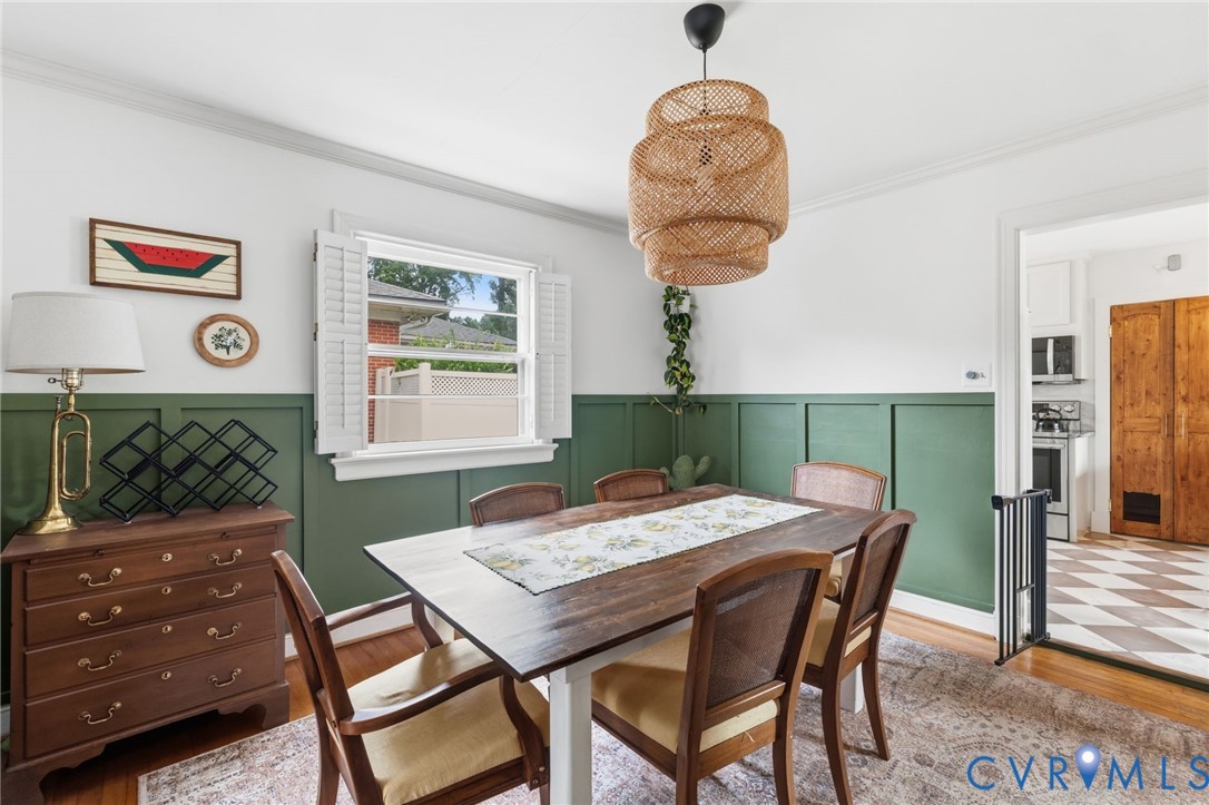 Dining area featuring a wainscoting accent wall, a multi-tiered wicker light fixture, and wood-finish flooring
