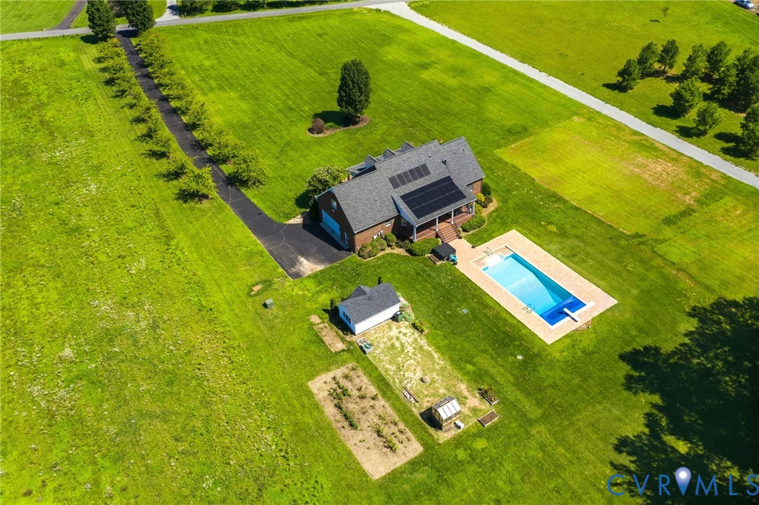 Expansive property featuring a brick residence with solar panels, a rectangular swimming pool with diving board, a separate outbuilding, a cultivated garden area, and a paved driveway lined with trees
