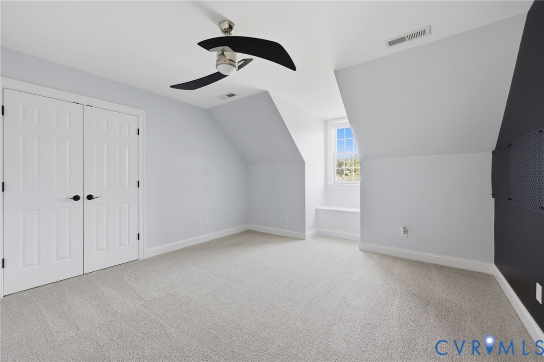 Spacious room featuring light-toned carpet, white double-door closet, modern ceiling fan, and a built-in window bench