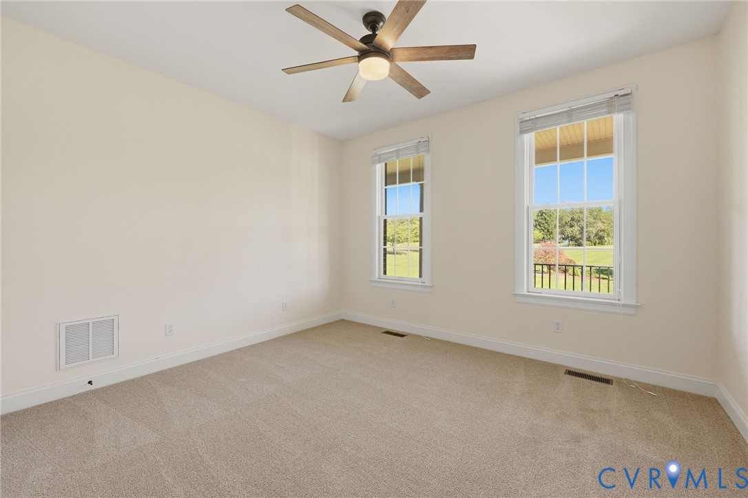 First Floor guest bedroom Light-filled room featuring two windows with white trim, tan carpeting, a ceiling fan with wood-finish blades, and neutral-toned walls