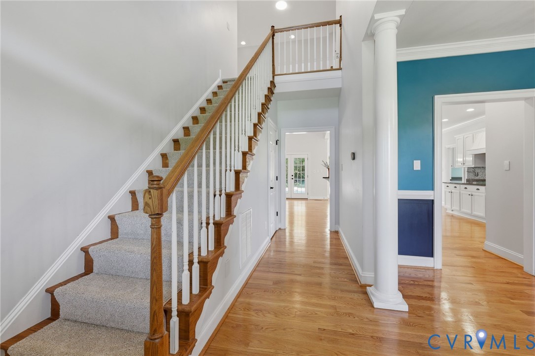 Foyer featuring hardwood flooring, a carpeted staircase with wood handrails and white balusters, a decorative column, and an upper-level landing