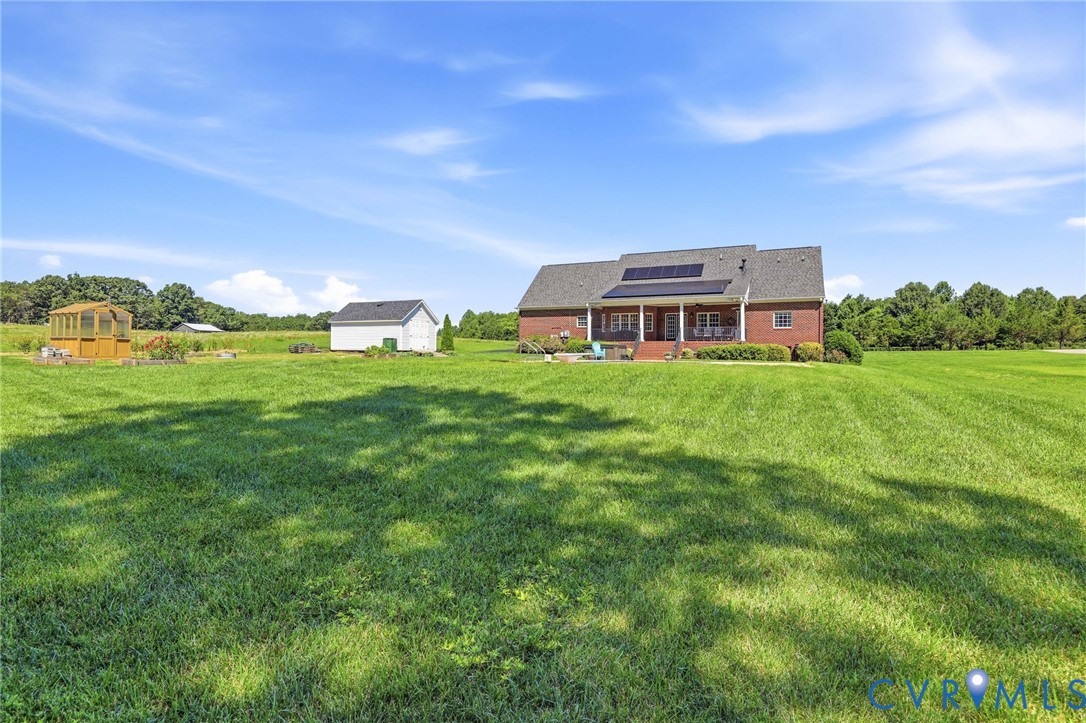 Expansive green lawn surrounds a brick residence featuring a covered patio, solar panels, and a detached storage building