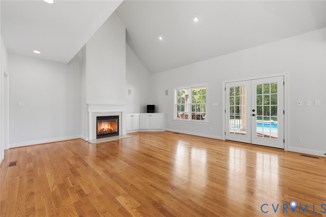 Living area featuring wood-finish flooring, a fireplace with a white mantel, vaulted ceilings, built-in cabinetry, and French doors opening to an outdoor pool