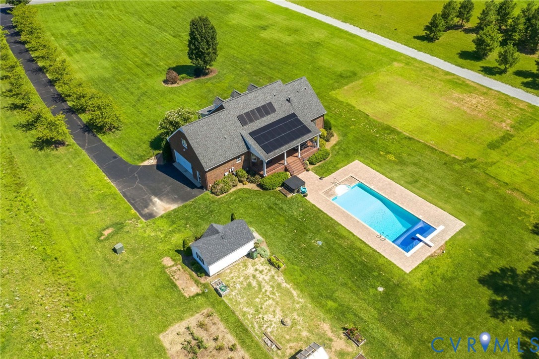 Expansive property featuring a brick residence with solar panels, a rectangular swimming pool with paved surround, a detached outbuilding, and a long paved driveway bordered by mature trees