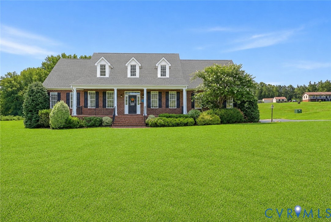 Traditional brick home featuring a covered front porch with white columns, black shutters, and three dormer windows Traditional brick home featuring a covered front porch with white columns, black shutters, and three dormer windows