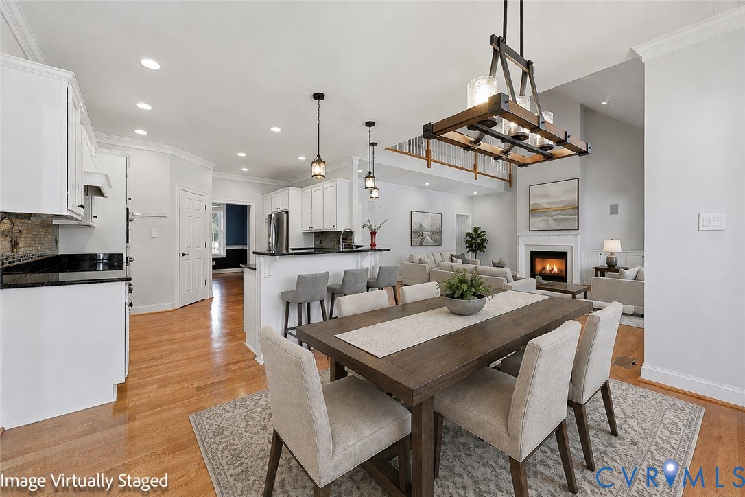 Open-concept design featuring wood-finish flooring, a kitchen with white cabinetry and dark countertops, and a living area with a fireplace