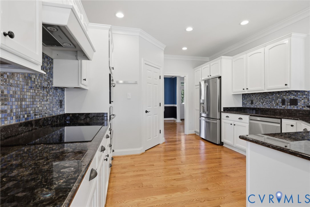 Kitchen featuring hardwood flooring, white cabinetry, dark stone countertops, stainless steel appliances, and a mosaic tile backsplash