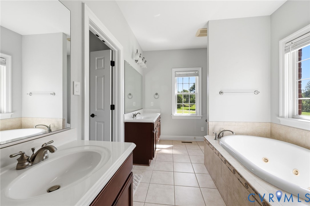 Bathroom featuring a jetted soaking tub with tiled surround, dual vanity with undermount sinks, and tile flooring