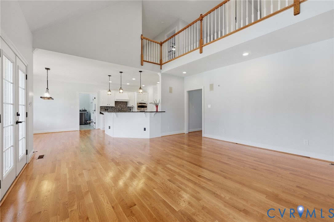 Expansive open-concept living area featuring wood-finish flooring, vaulted ceilings, and a second-story overlook with a wood railing