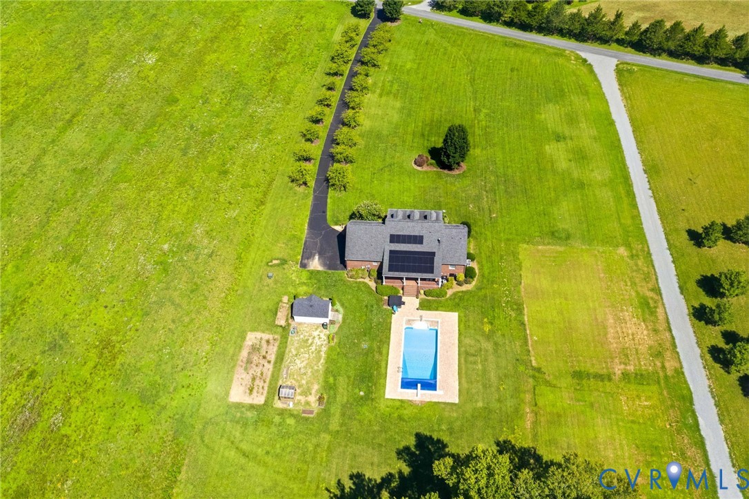 Expansive property featuring a brick residence with a dark shingle roof, solar panels, and a rectangular swimming pool with surrounding deck