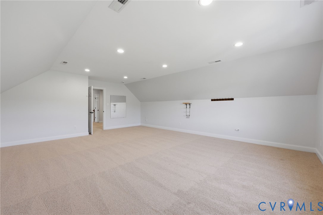Spacious carpeted room featuring vaulted ceilings, recessed lighting, and white baseboards