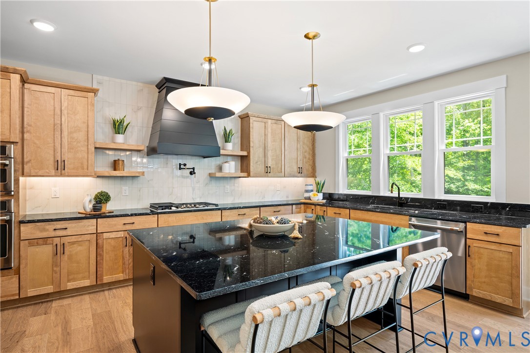 Kitchen featuring a large black stone-finish island with seating, natural wood cabinetry, a tiled backsplash, and recessed lighting
