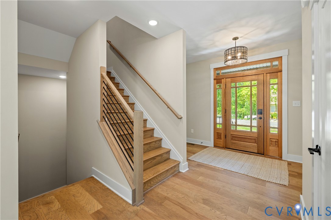 Foyer featuring a wooden front door with glass panels and sidelights, wood-finish flooring, a contemporary chandelier, a staircase with wood treads and a metal railing system, and recessed lighting