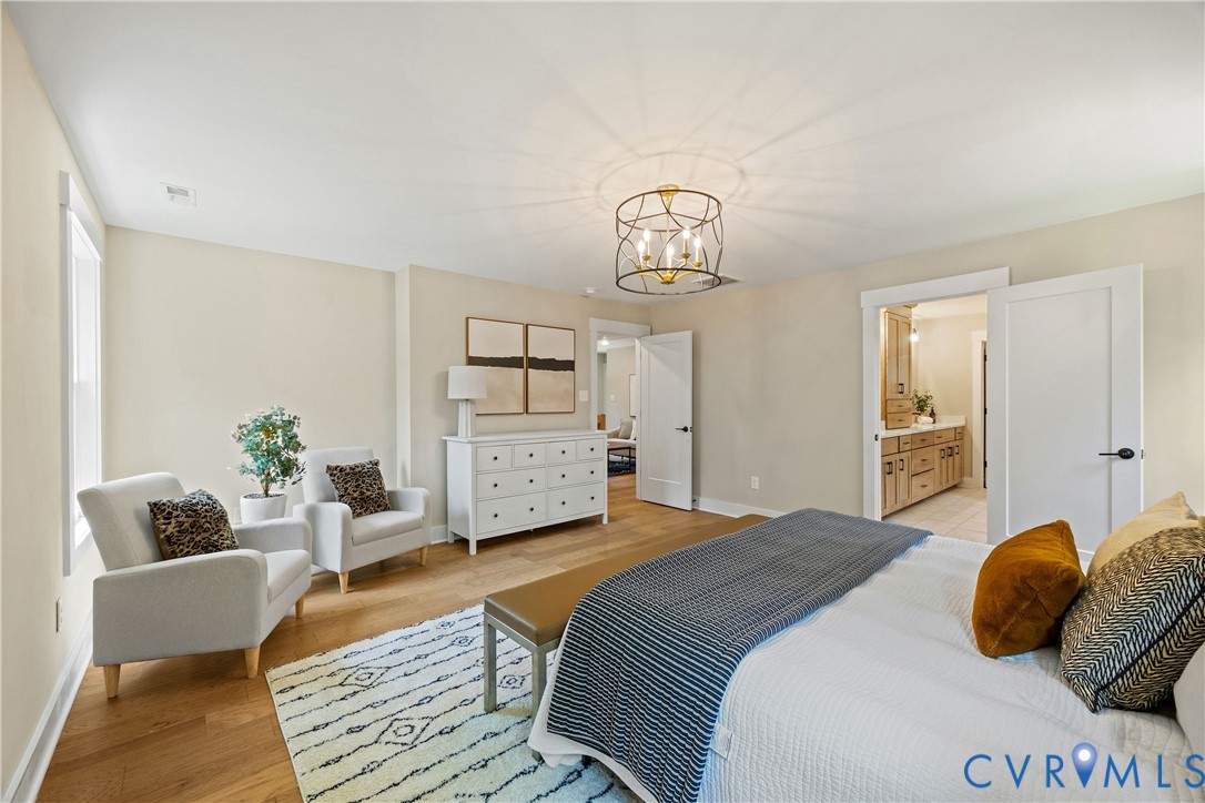 Spacious room featuring wood-finish flooring, a contemporary chandelier, two panel doors, and a bathroom with a double vanity