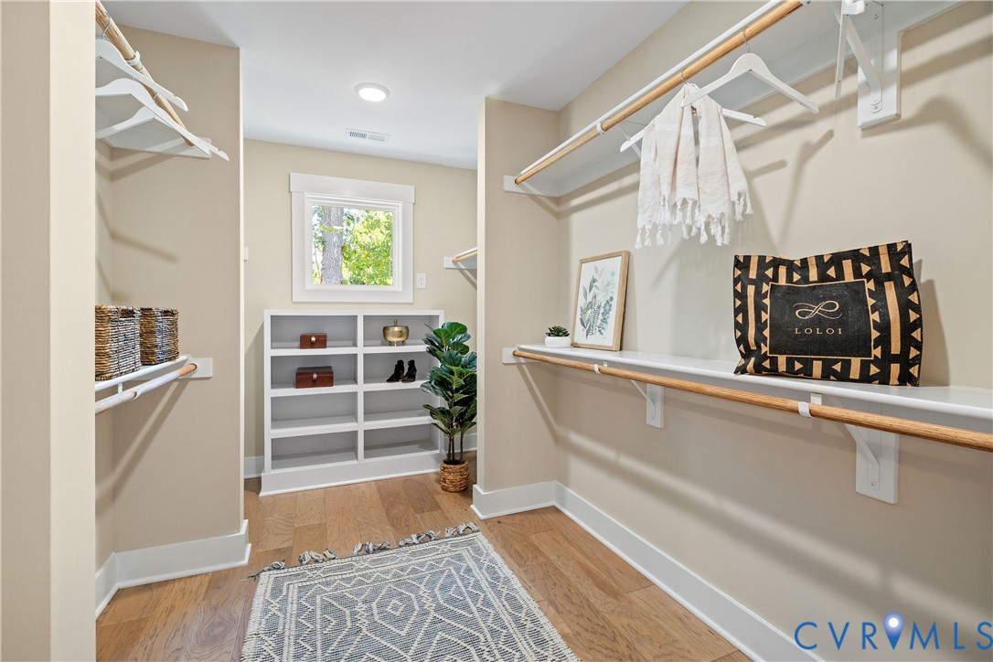 Organized closet space featuring wood-finish flooring, built-in shelving, and a window for natural light