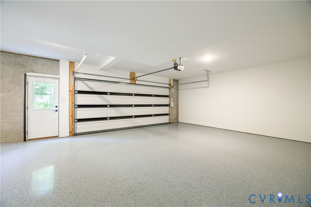 Spacious garage featuring an epoxy-coated concrete floor, an automatic overhead door, and a separate side entry door with clear glass