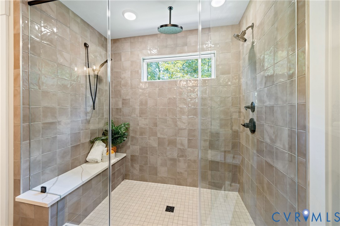 Spacious shower enclosure featuring full-height tiled walls, a built-in bench with a light-toned surface, a rainfall showerhead, and an additional wall-mounted showerhead