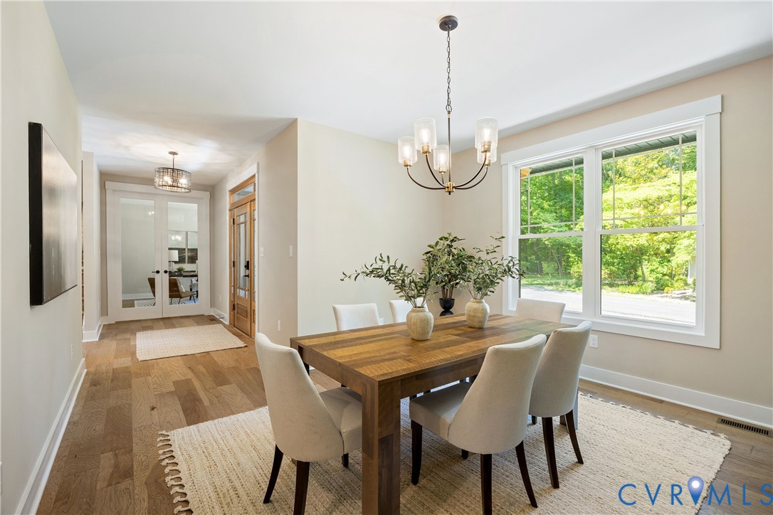 Open-concept dining area featuring wood-finish flooring, a contemporary chandelier, large windows, and a clear sightline into a separate room through glass-paneled double doors