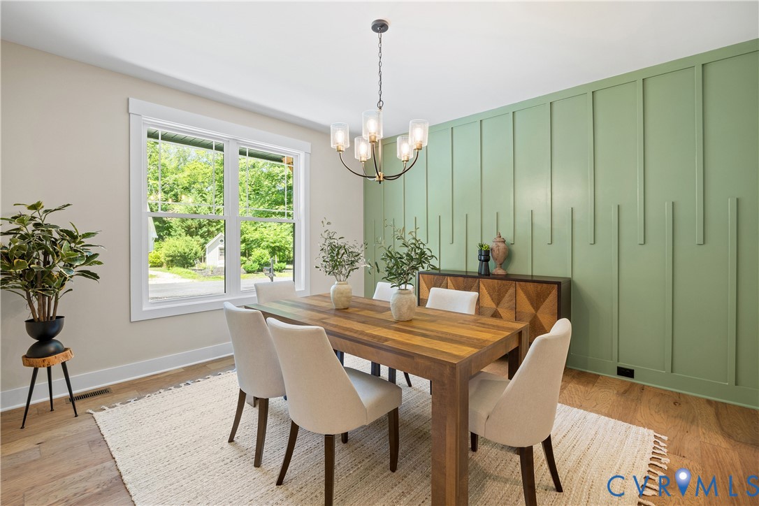 Dining area featuring a decorative accent wall with vertical paneling, hardwood flooring, and a contemporary chandelier