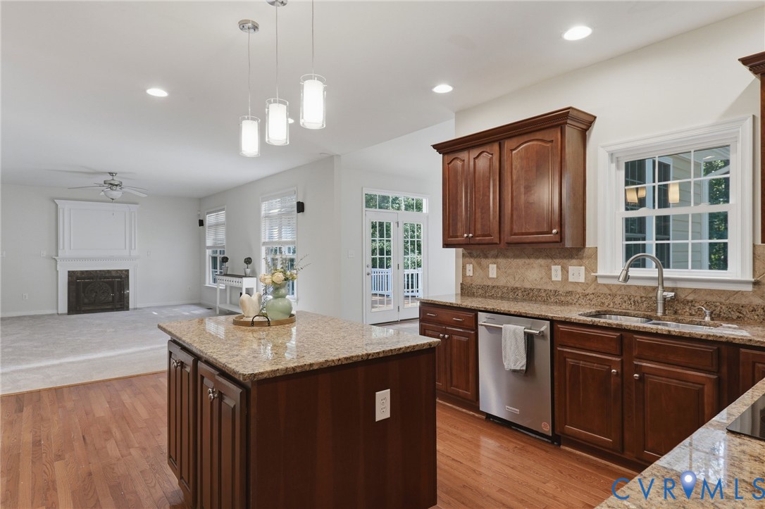 Kitchen island with granite countertop, wood-finish flooring, stainless steel dishwasher, wood cabinetry, and recessed lighting