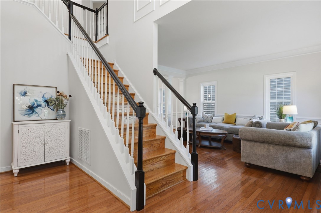Hardwood flooring throughout, a two-story foyer, a staircase with white risers and dark wood handrails, and a living area with multiple windows