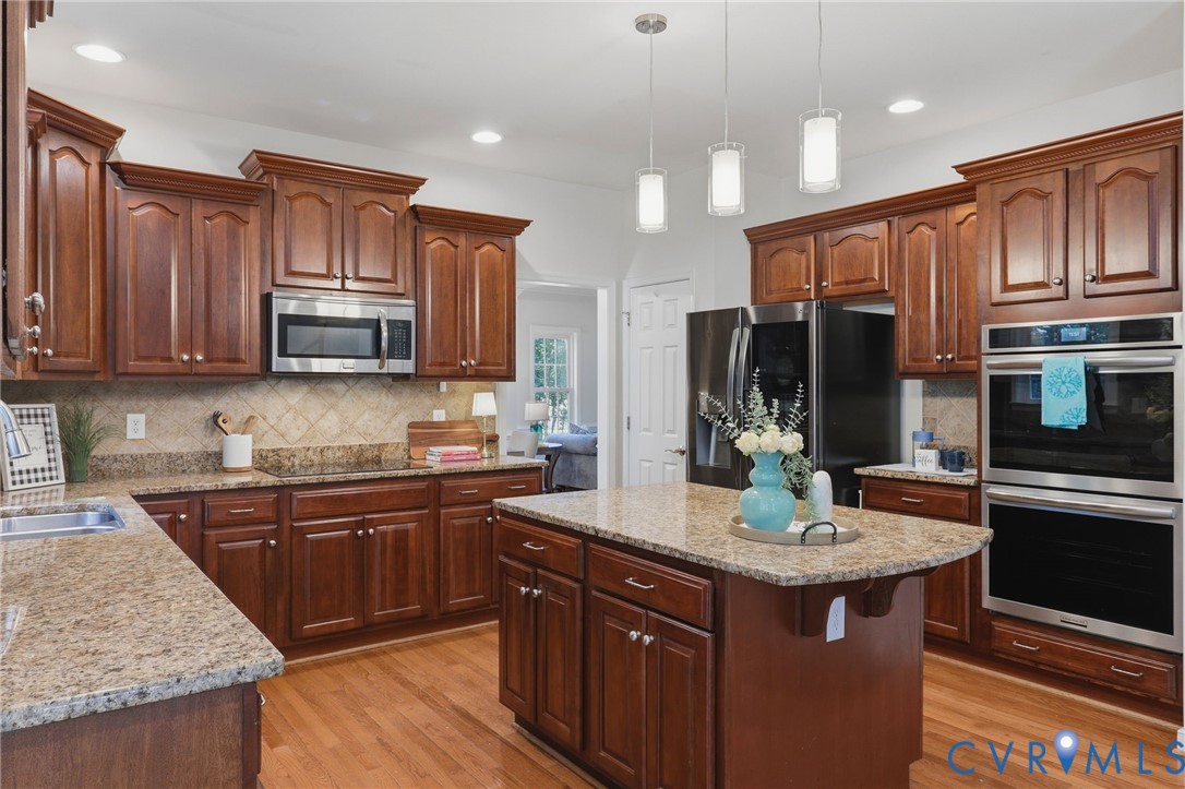 Hardwood flooring, wood cabinetry, granite countertops, stainless steel appliances, and a central island with pendant lighting