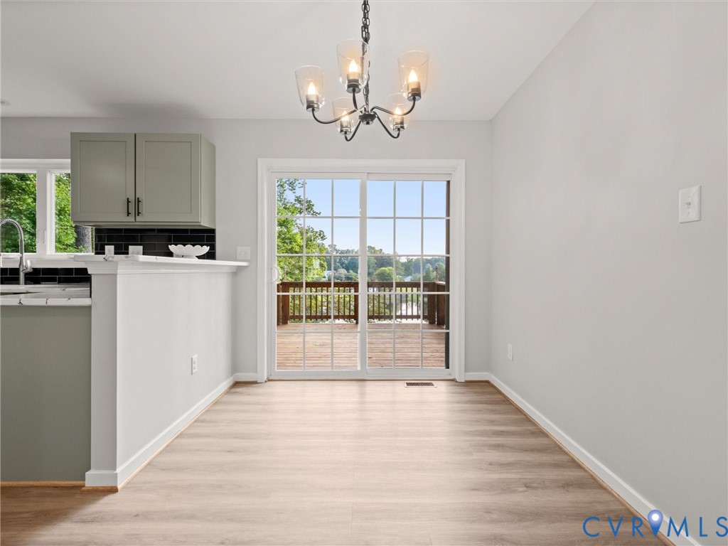 Light wood-finish flooring, glass-paned sliding door, black subway tile backsplash, and a black wrought iron chandelier with clear glass shades