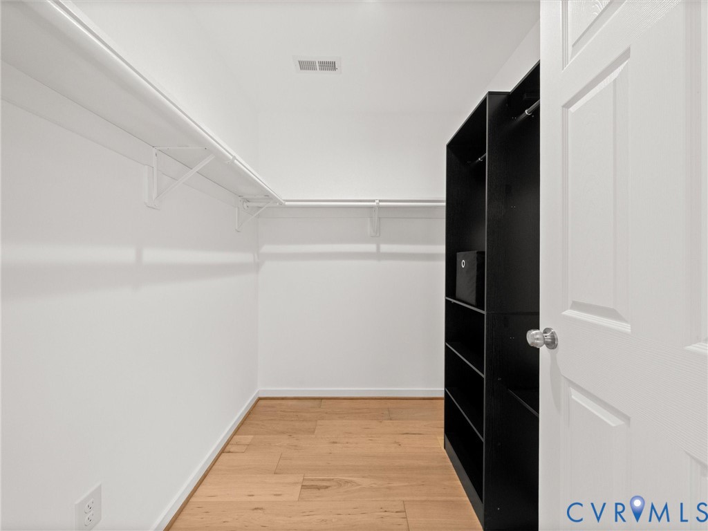 Walk-in closet featuring wood-finish flooring, built-in shelving, and white walls