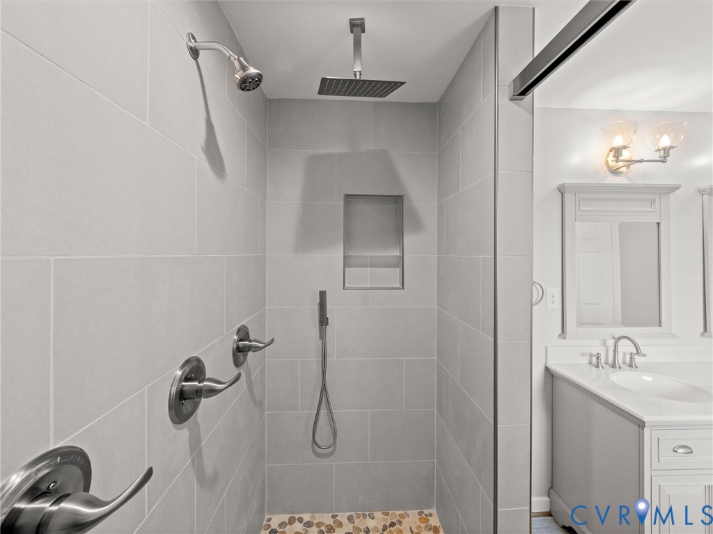 Shower featuring light-toned tile walls, a built-in niche, a rainfall showerhead, and a handheld shower attachment