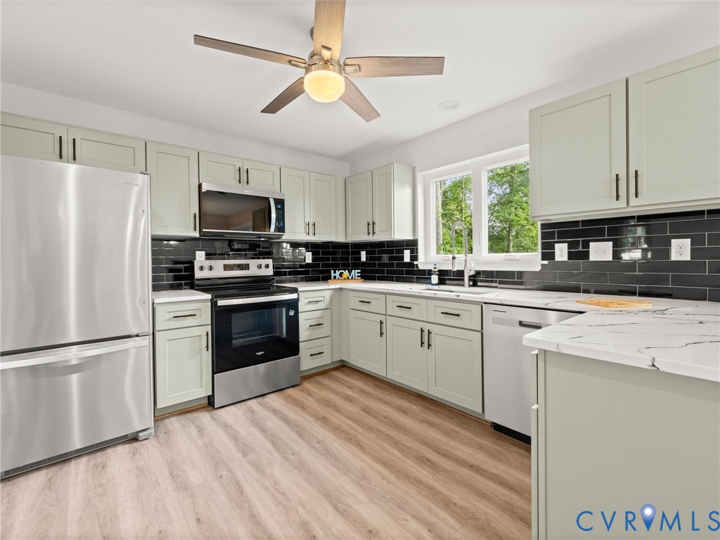 Kitchen featuring stainless steel appliances, light-toned cabinetry, a black subway tile backsplash, white countertops, and wood-finish flooring