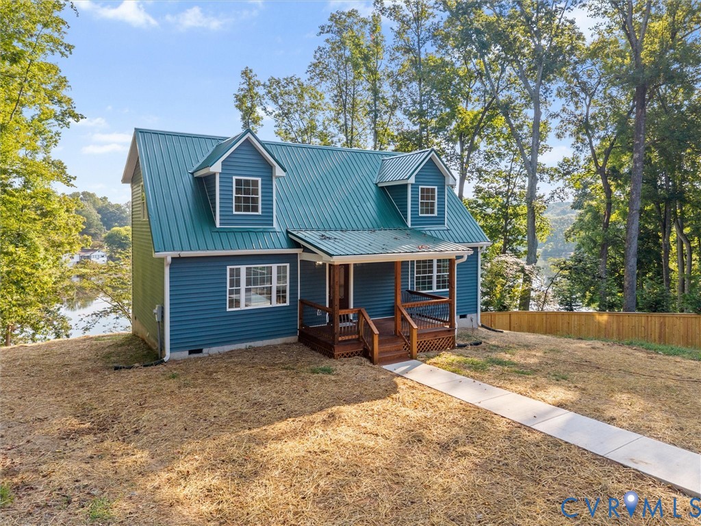 Blue siding exterior featuring a green metal roof, a covered porch with wood railings, and multiple dormer windows