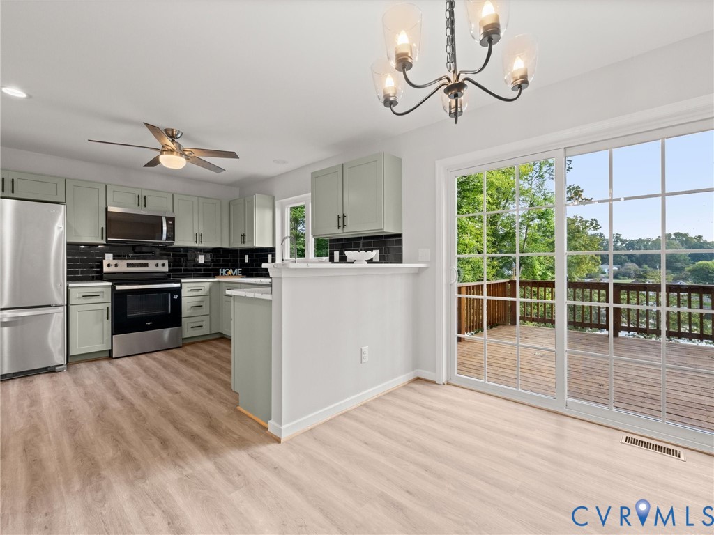 Kitchen featuring sage cabinetry, stainless steel appliances, black subway tile backsplash, and light wood-finish flooring